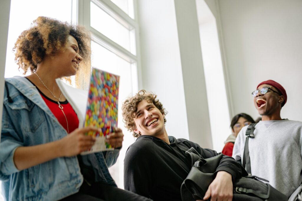 A group of cheerful students laughing and socializing in a bright college corridor.